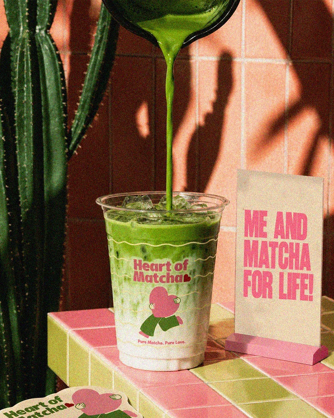 Clear iced Heart of Matcha cup printed with Pure Matcha. Pure Love. on a pink and green tiled counter. Cup design by LIRCLE