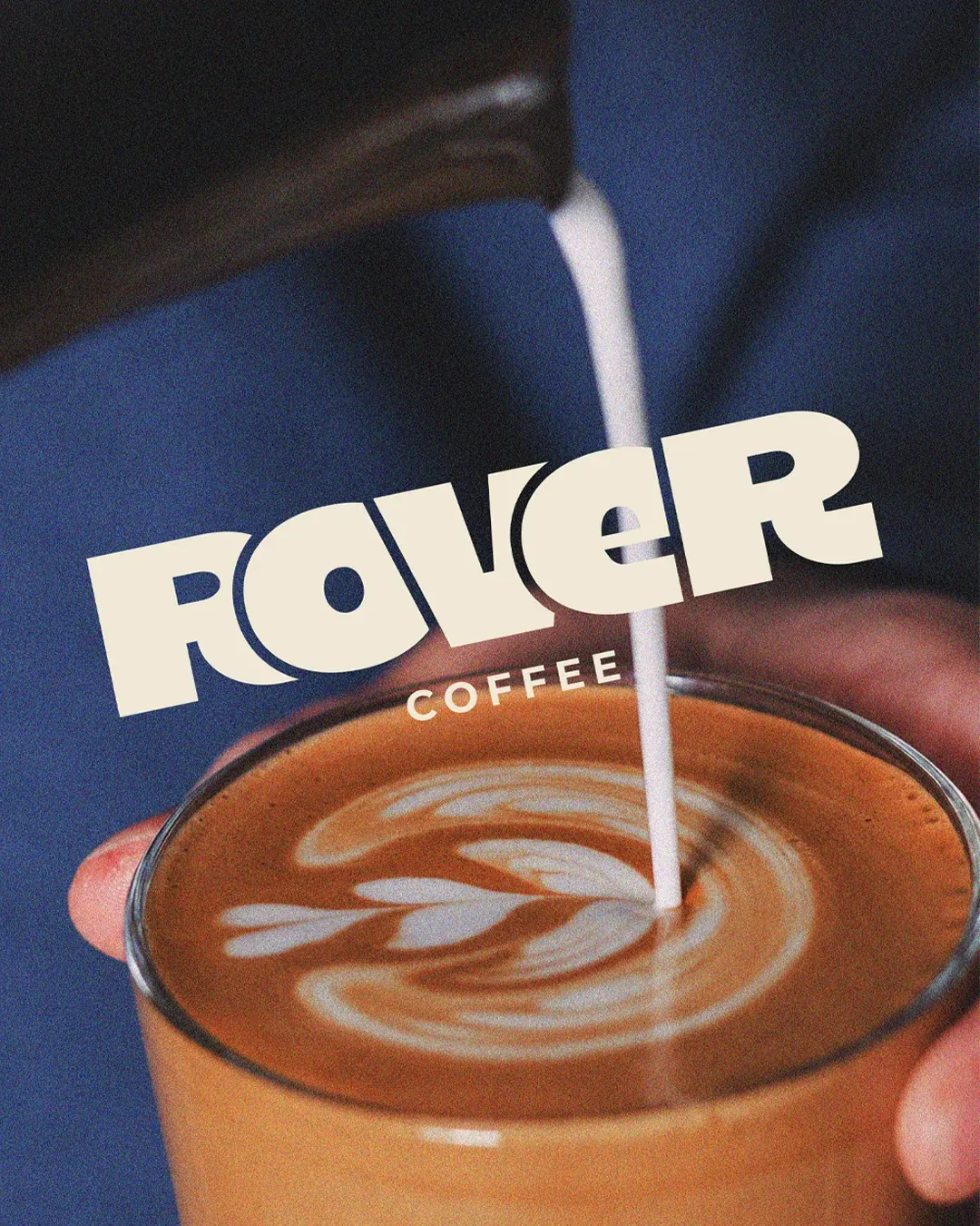 Rover Coffee wordmark in cream over milk being poured into a latte on navy. Coffee logo design by LIRCLE